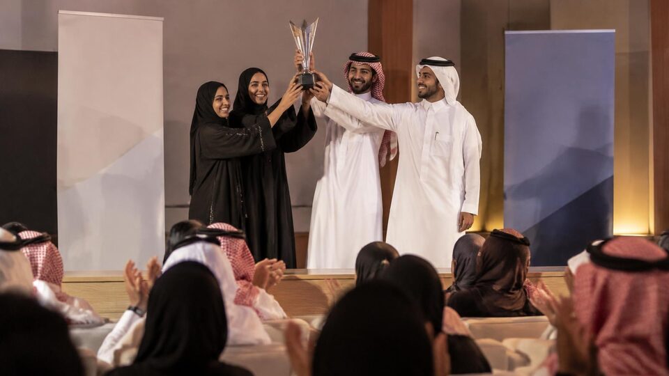 فريق طلابي يرفع كأسًا على مسرح في فعالية جامعية بحضور جمهور